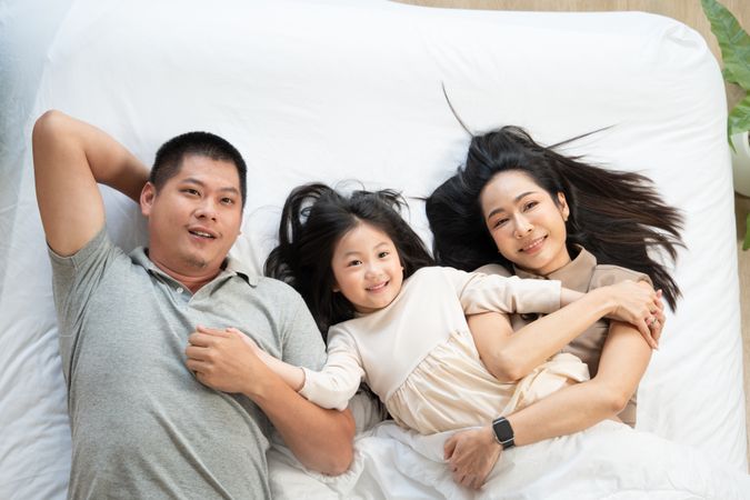 Top view of Asian family lying on bed and holding hands together.