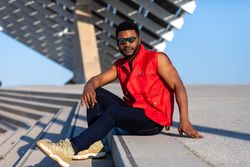 Black man sitting on stairs outside in vest and sunglasses