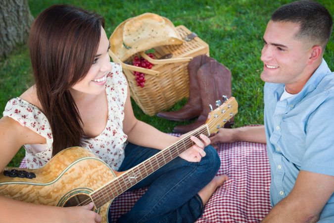 Young Adult Female Playing Guitar with Boyfriend In The Park.