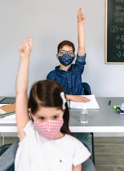 Students with masks raising hands at school
