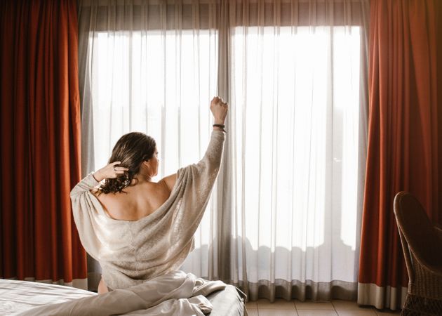 Woman waking up and stretching arms while sitting on bed