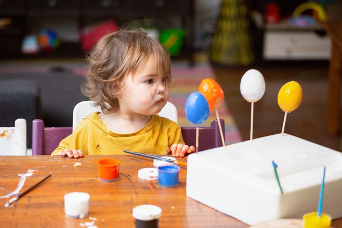 Toddler girl painting egg at table