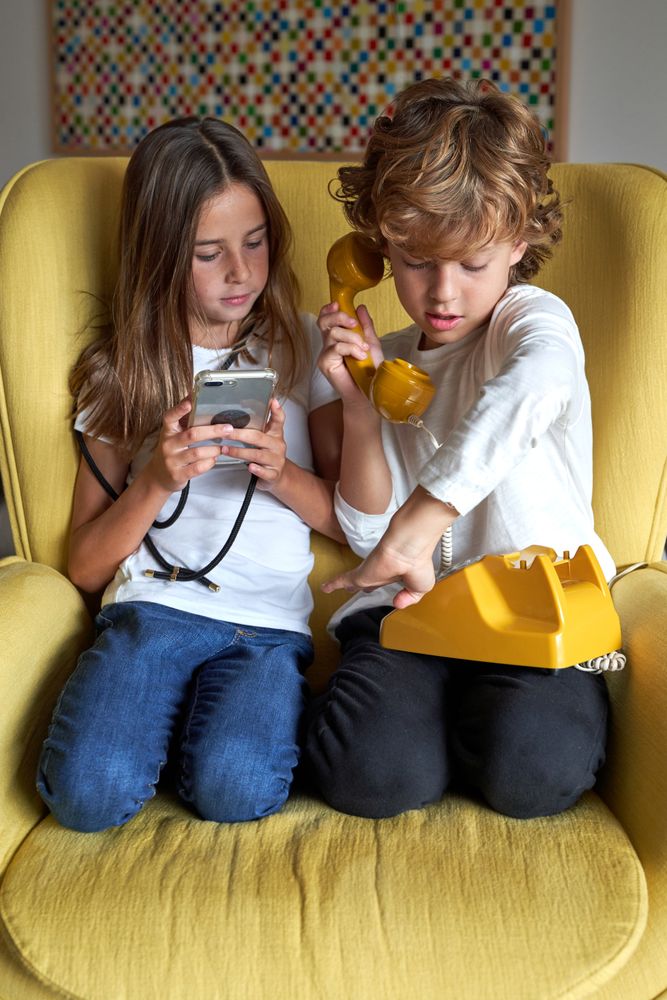 Girl with smartphone near boy with retro telephone