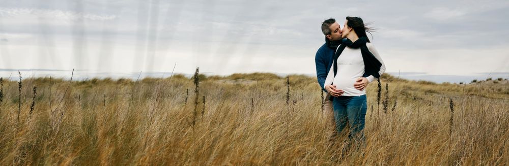 Pregnant woman with partner kissing and holding belly