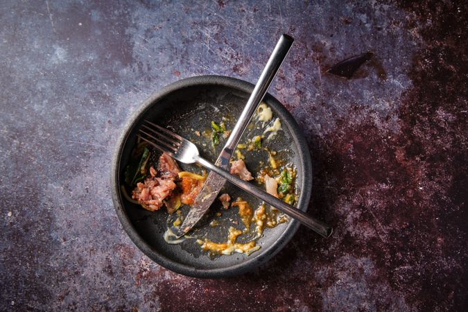 Fork and knife on black plate with food leftovers