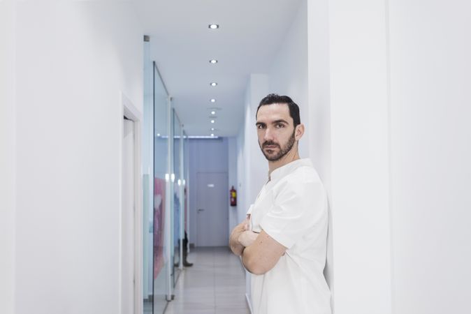 Side view portrait of a bearded doctor standing in the hospital hallway while looking camera