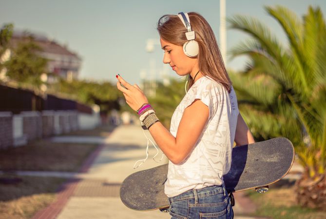 Young girl with skateboard and headphones listening music outdoors
