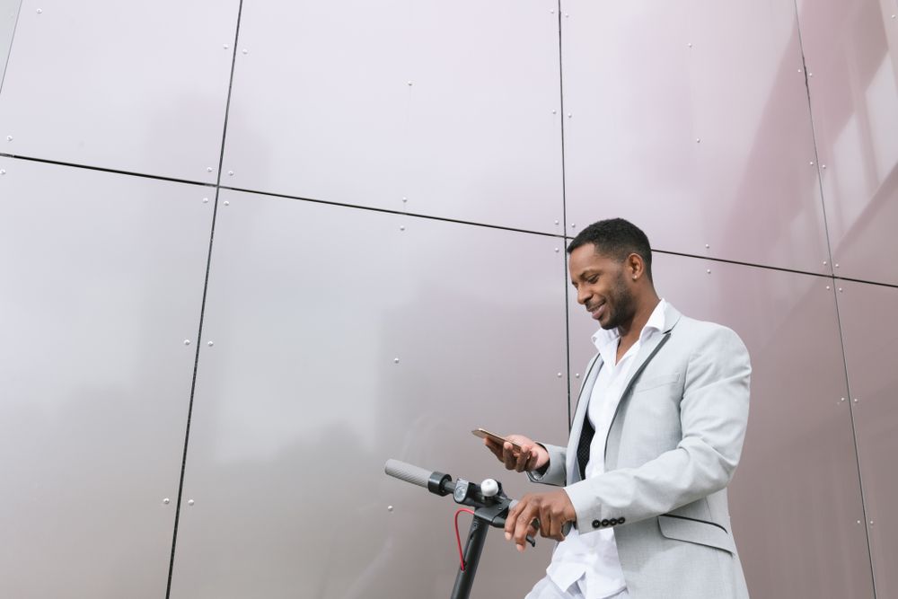Smiling Black man riding scooter and speaking on smartphone