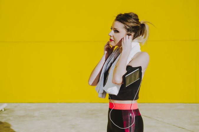 Woman with earphones running near wall