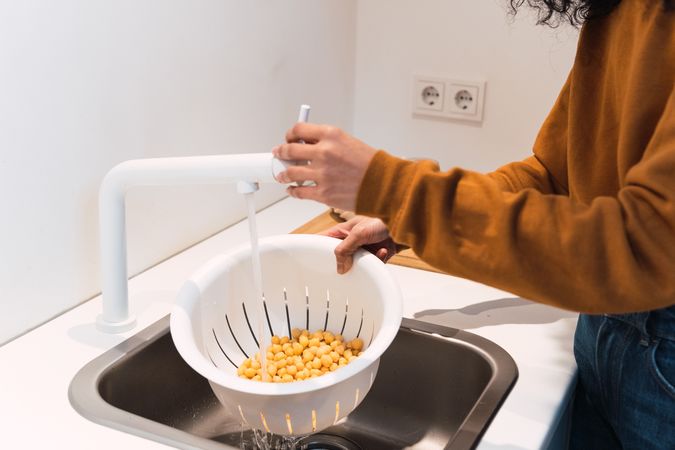 Crop woman washing chickpeas in sink