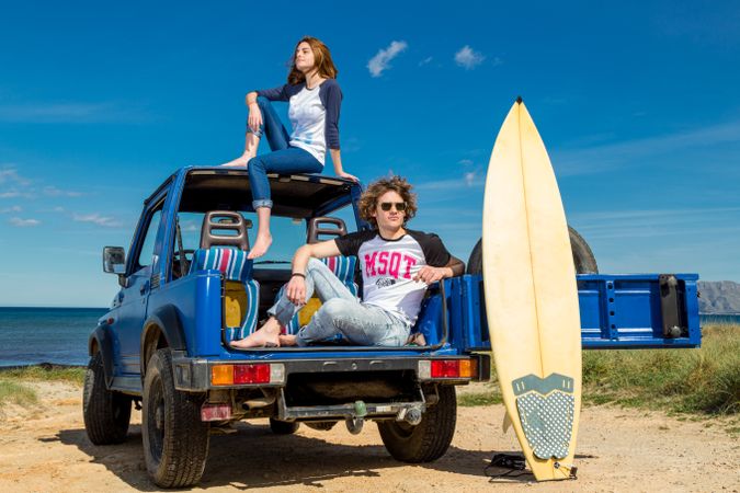 Guy with surfboard and woman on roof of car