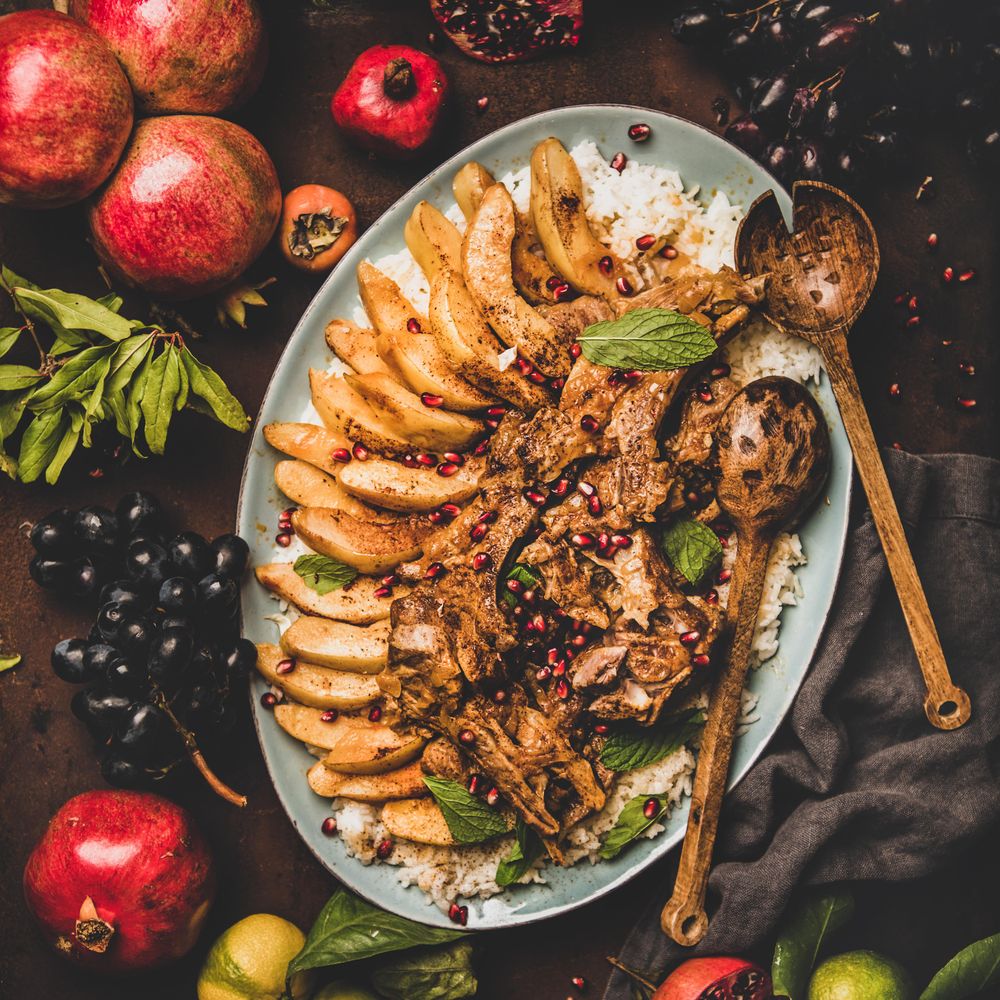 Plate of lamp chops over rice, and quince on table with grapes and pomegranate, square crop