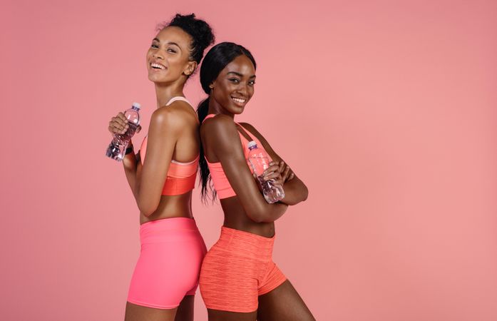 Fitness women relaxing after workout against pink background