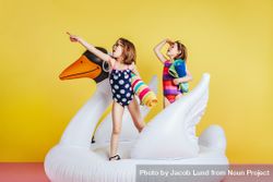 Twin girls having fun on inflatable toy flamingo over yellow background 5o1E1b
