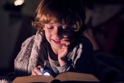 Positive boy reading book in darkness