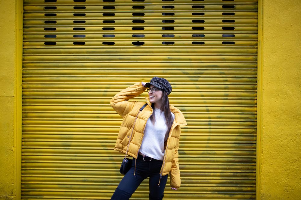 Trendy female standing near yellow wall on street