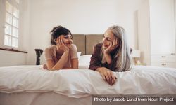 Mother and daughter on bed looking at each other lying on bed with their heads resting on palms 4j6E94
