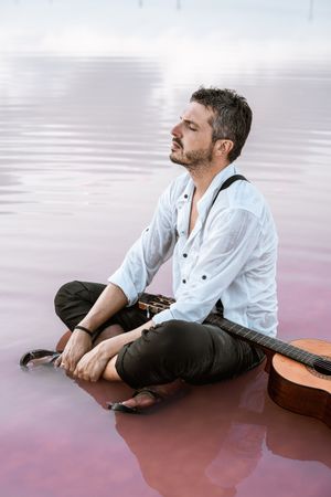 Musician with guitar on pink sandy water