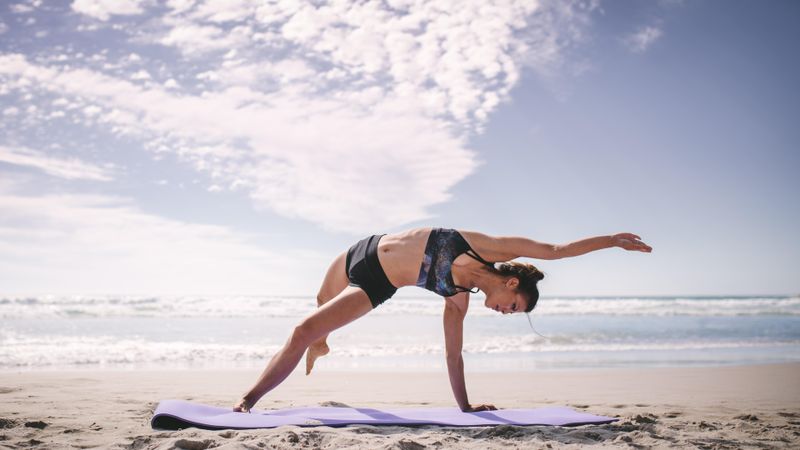 Flexible woman doing yoga exercise outdoors on the beach