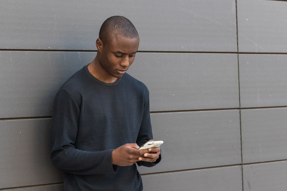 Serious Black man using smartphone against gray wall