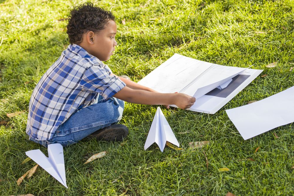 Boy Learning How to Fold Paper Airplanes on the Grass