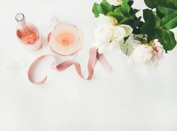 Glass of pink rose wine, and bottle with flowers and ribbon, horizontal composition with copy space