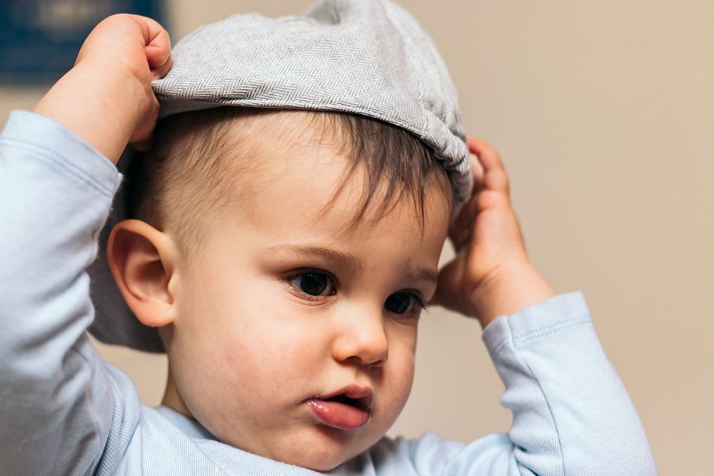 cute baby putting on a hat at home
