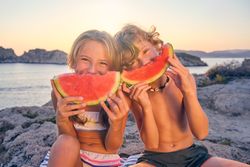 Cheerful kids eating watermelon on summer beach