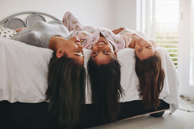 Young women lying on edge of bed with their hair hanging down