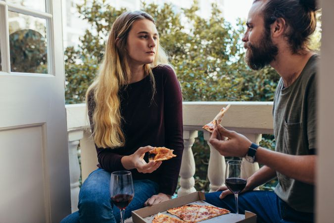 Couple sharing a pizza sitting in the balcony of their apartment