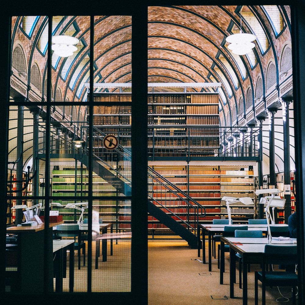 an opened door of a beautiful library with spring-color arranged of books in the bookshelves inside.