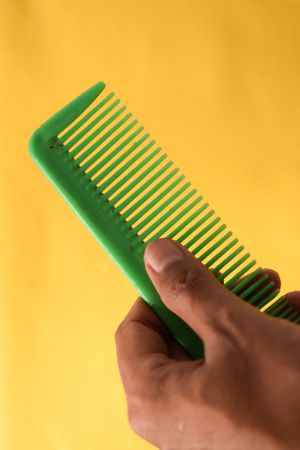 Hand holding bright green hair comb diagonally against yellow background
