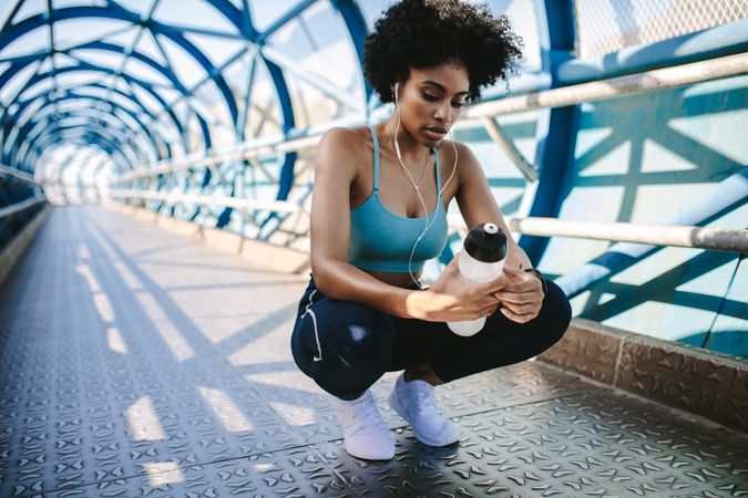 Female in sportswear crouching on a bridge with water bottle