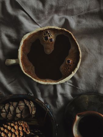 Coffee cup and pinecones on grey bed sheets
