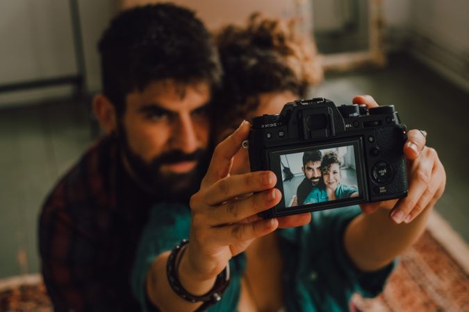 Joyful couple embracing and taking selfie on camera at home