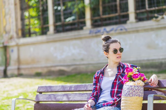 Front view of a young hipster woman sitting on a park bench relaxing in a sunny day while using a mobile phone