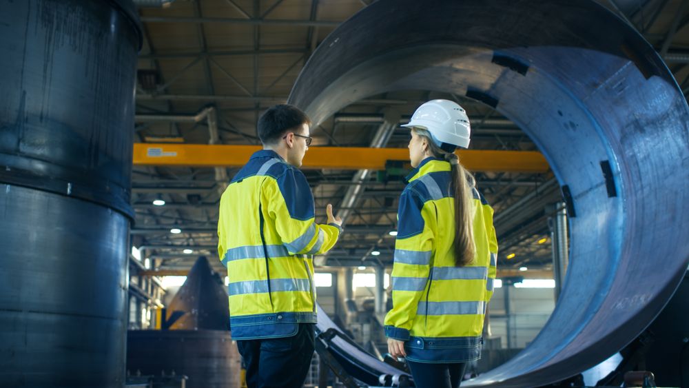 Male Industrial Worker and Female Chief Engineer in a Hard Hat Discuss Metalworking Factory's New Project.