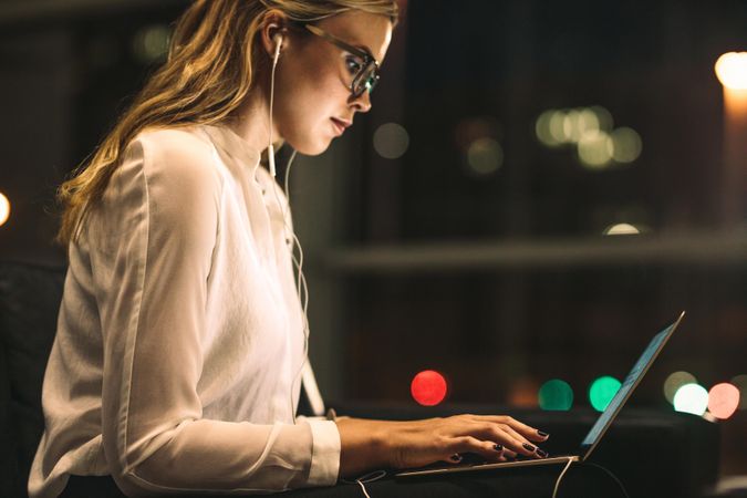 Side view of businesswoman using laptop in office lobby at night