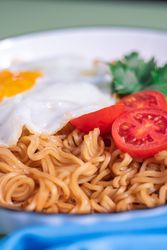 A plate of noodles with an egg and tomato on top