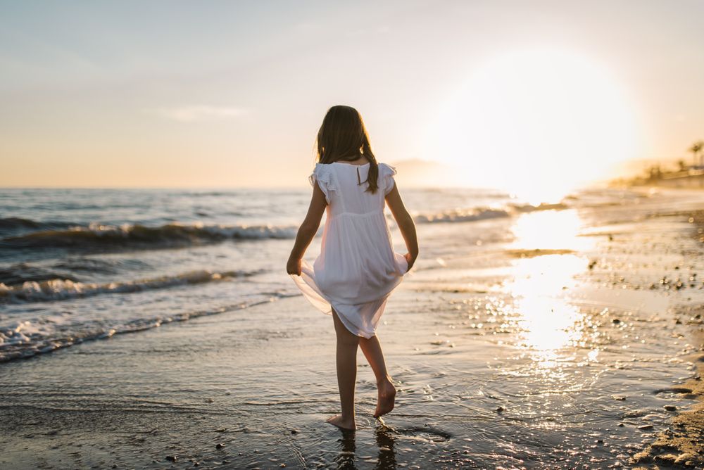 Adorable girl walking on seaside at sunset