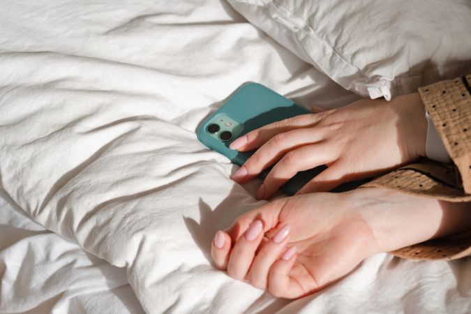 Hand holding smartphone on bed