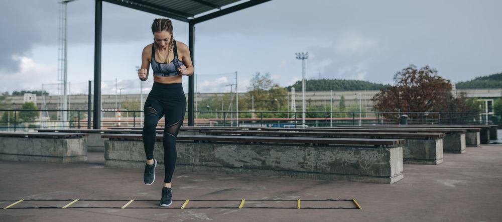 Sportswoman jumping on an agility ladder