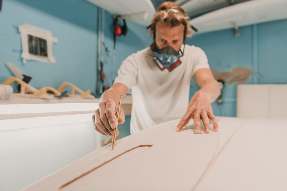 Man in respirator measuring surf board in workshop