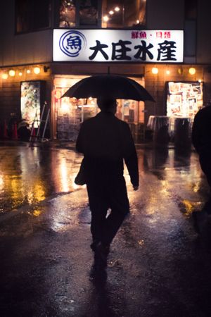 Silhouette of a man holding an umbrella walking down the street during night