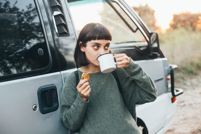 Woman leaning on camper van sipping coffee