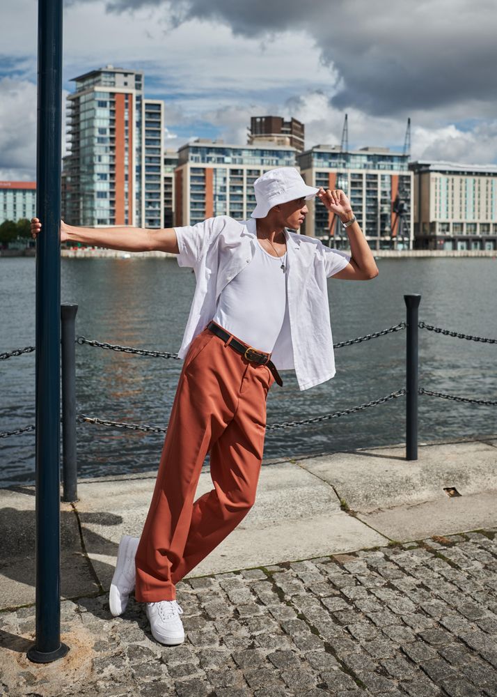 Stylish young man in hat hanging onto a streetlamp on the waterfront