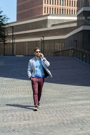 Young bearded man walking in the sun while talking on mobile phone
