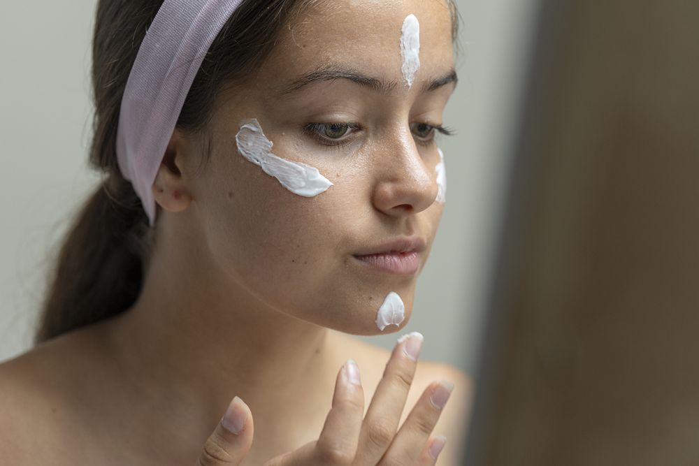 Young woman applying dots of face cream or foundation before blending, skincare routine