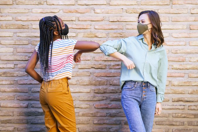 Female friends tapping elbows instead of shaking hands in front of brick wall
