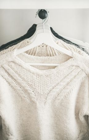 Close up of knitted sweaters on hangers, light background, vertical composition